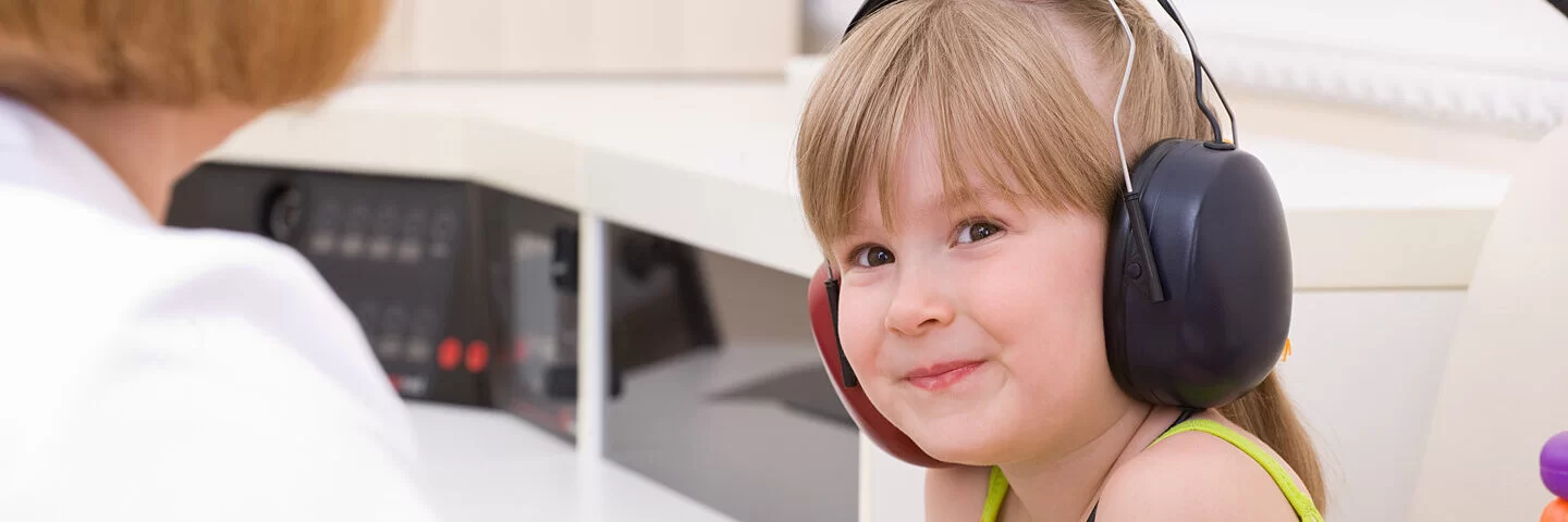 Eine Ärztin prüft das Gehör eines kleinen Mädchens, das beim Test Kopfhörer trägt.