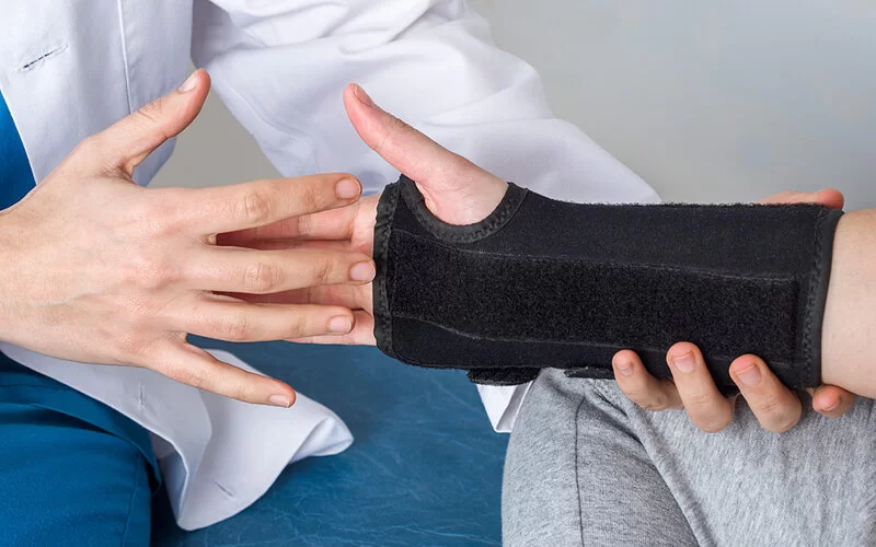 Patientin oder Patient mit Karpaltunnelsyndrom bekommt eine Bandage ans Handgelenk angelegt.