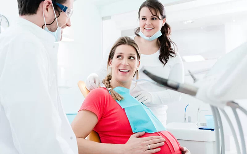 Schwangere Frau sitzt auf dem Behandlungsstuhl beim Zahnarzt.
