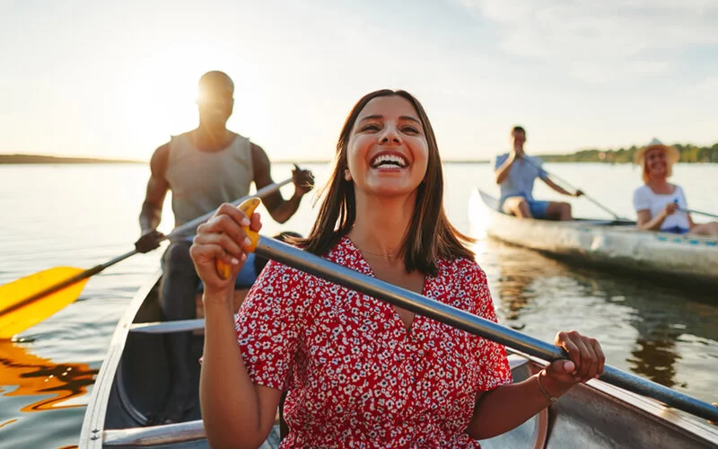 Eine Frau sitzt in einem Kanu und hält lachend ein Paddel in der Hand.