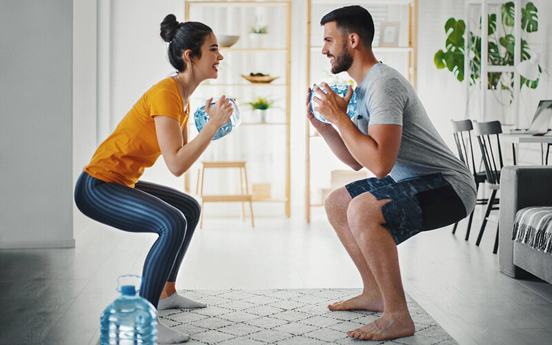 Anstelle von Hanteln nutzt ein Paar für ihr Workout im Wohnzimmer Wasserflaschen für den Muskelaufbau.