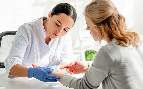 Eine Dermatologin untersucht eine Patientin auf Kleienpilzflechte (Pityriasis versicolor) am Unterarm.