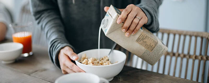 Eine Frau gießt sich Mandelmilch auf ihr Müsli.