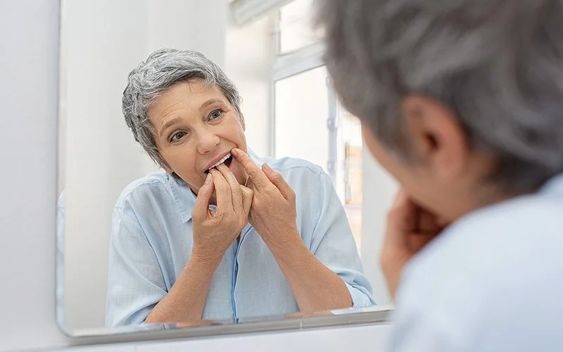 Eine Frau reinigt sich ihre Zähne vor dem Spiegel mit Zahnseide.