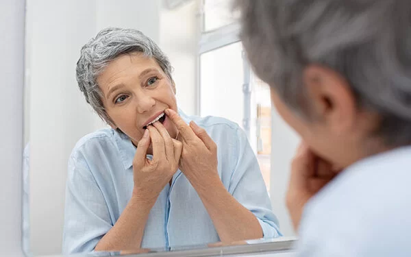 Eine Frau reinigt sich ihre Zähne vor dem Spiegel mit Zahnseide.