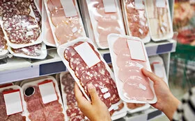 Frau im Supermarkt hält zwei unterschiedliche Sorten abgepackten Wurstaufschnitts.