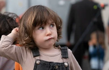 Ein Kleinkind mit braunen Haaren in einem Jeansoverall schaut zur Seite.