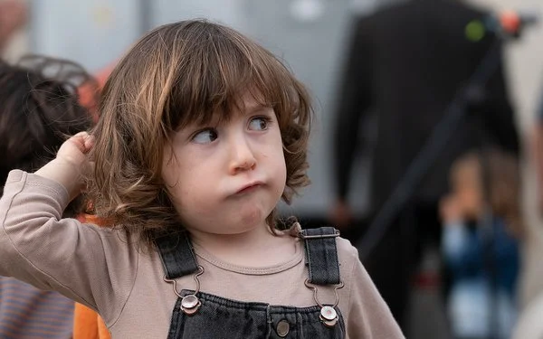 Ein Kleinkind mit braunen Haaren in einem Jeansoverall schaut zur Seite.