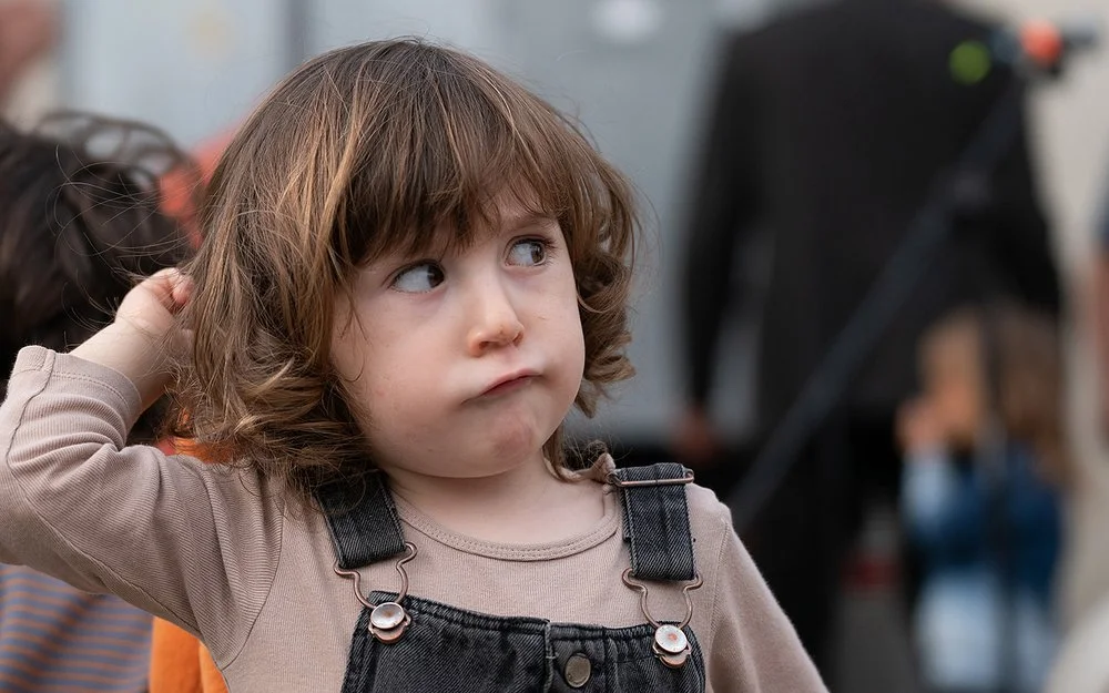 Ein Kleinkind mit braunen Haaren in einem Jeansoverall schaut zur Seite.