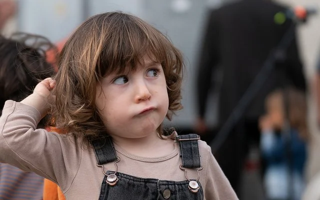 Ein Kleinkind mit braunen Haaren in einem Jeansoverall schaut zur Seite.