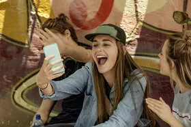 Eine Jugendliche ist von ihren Freunden umgeben und lacht ihr Smartphone an.
