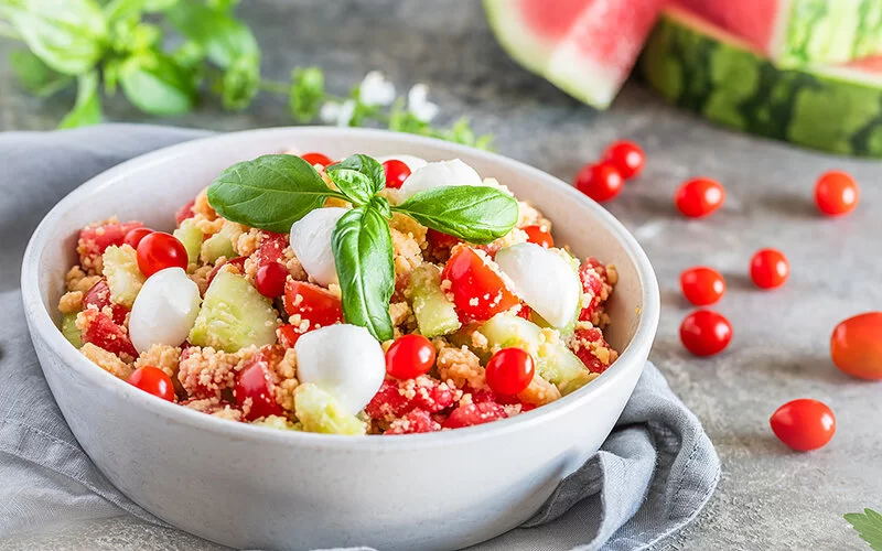 Frischer Couscous-Salat mit Tomaten, Mozzarella, Gurken und Basilikum in einer Schüssel.