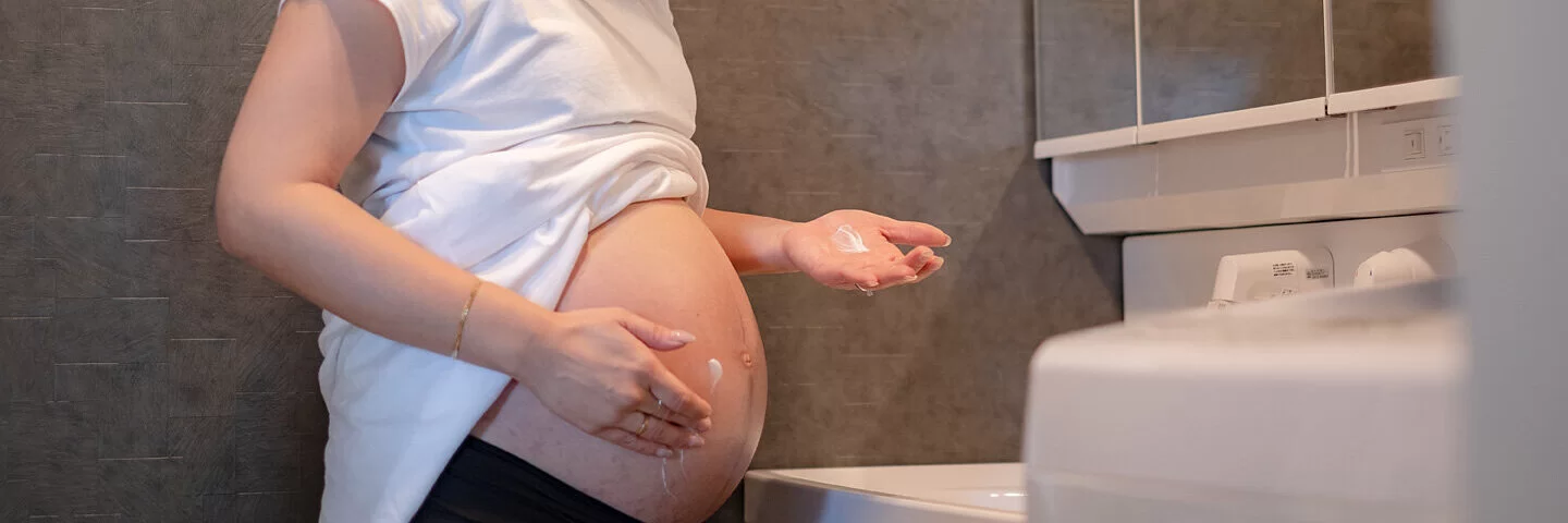 Eine schwangere Frau schmiert Creme auf ihren Bauch, um Dehnungsstreifen zu verhindern.