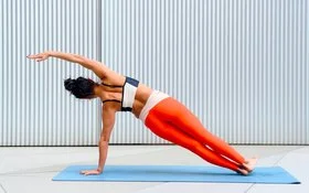 Eine Frau führt die Seitenplanke auf einer Yogamatten aus.