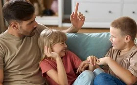 Ein Mann und eine Frau mit zwei Kindern im Teenageralter sitzen zusammen auf dem Sofa. Die Kinder albern übermütig herum, die Erwachsenen schauen ernst und angespannt.