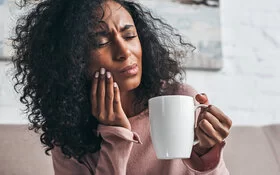 Eine Frau hat Zahnschmerzen nach einer Weisheitszahn-OP und hält eine Tasse mit Tee in der Hand.