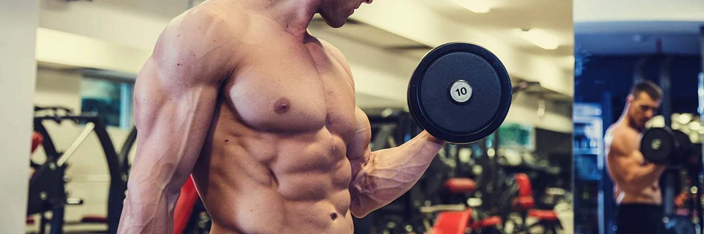 Ein junger Bodybuilder mit freiem, muskulösen Oberkörper macht einen Bizepscurl mit einer Kurzhantel.