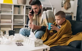 Vater und Sohn haben einen Atemwegsinfekt und ruhen sich gemeinsam auf dem Sofa aus. 