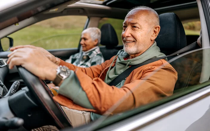 Ein Seniorenpaar sitzt angeschnallt im Auto, er hinterm Lenkrad und sie auf dem Beifahrersitz.