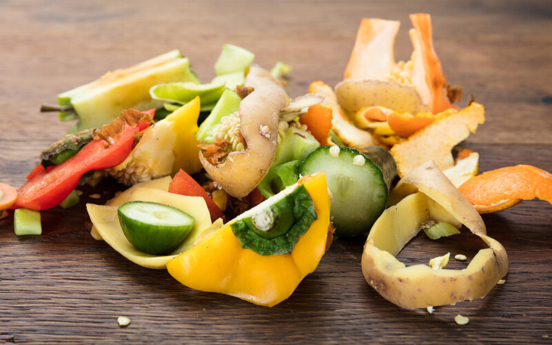 Gemüsereste von Paprika, Zucchini und Kartoffelschalen liegen auf einem Holzbrett.