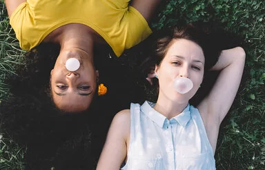 Zwei Teenager liegen auf einer Wiese und pusten Kaugummi-Blasen auf.