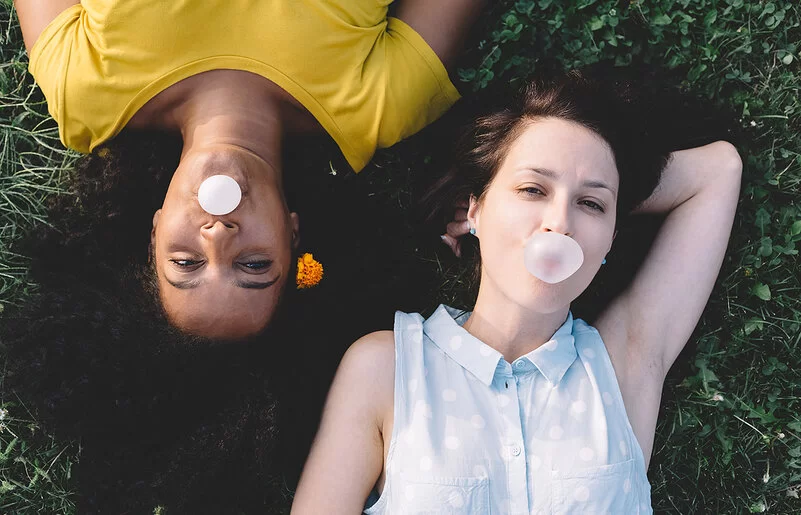 Zwei Teenager liegen auf einer Wiese und pusten Kaugummi-Blasen auf.