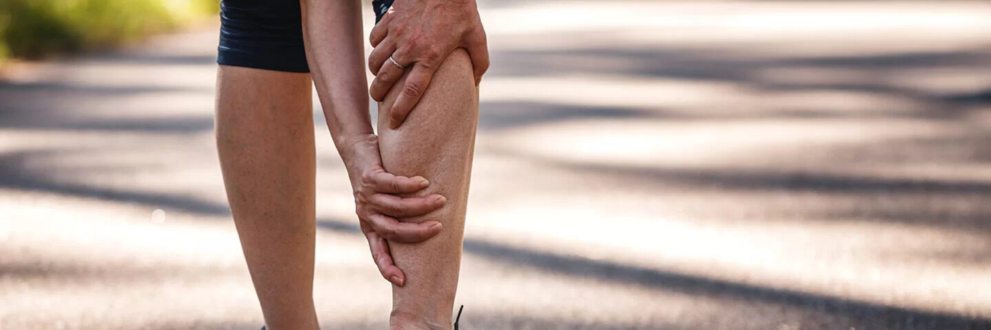 Eine Joggerin mit Magnesiummangel hat einen Wadenkrampf und hält sich das Bein.