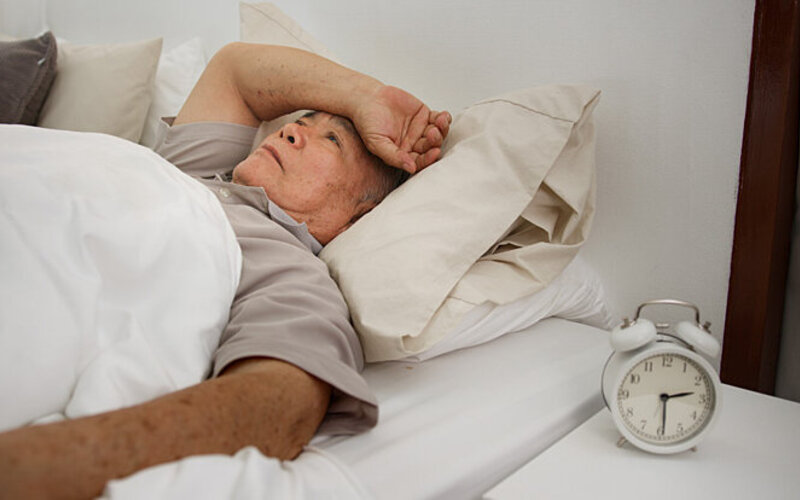 Ein Mann liegt wach im Bett und leidet unter Schlaflosigkeit – einem Symptom von Stress.