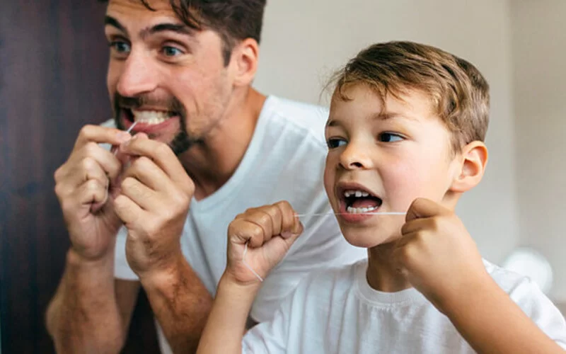 Eine Junge und ein Vater reinigen ihre Zahnzwischenräume mit Zahnseide.