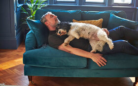 Bewegungsmuffel liegt mit seinem Hund auf der Couch und braucht Tipps für mehr Bewegung im Alltag.