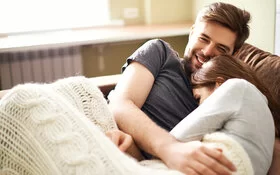 Junges Paar kuschelt gemütlich auf dem Sofa und einer Decke.