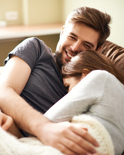 Junges Paar kuschelt gemütlich auf dem Sofa und einer Decke.