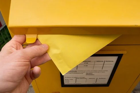 Eine Person steckt einen Umschlag in einen Briefkasten.