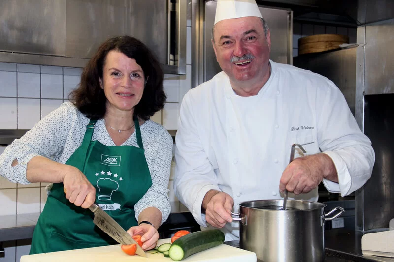 Die Moderatoren der AOK-Kochshow in Heidenheim stehen in der Küche und schauen in die Kamera.