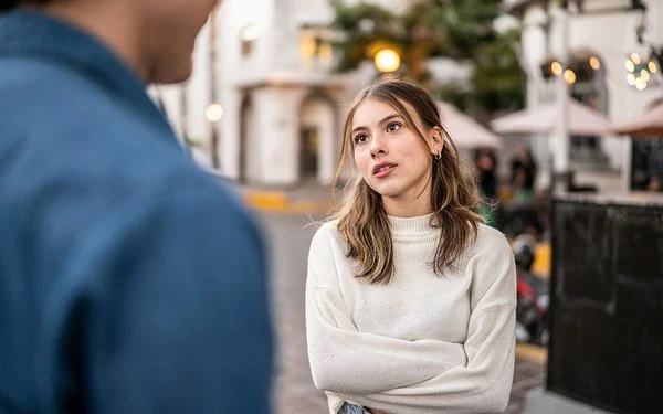 Ein junges Paar streitet sich im Freien. Die Körpersprache und der Gesichtsausdruck der Frau deuten auf Wut oder Frustration hin.