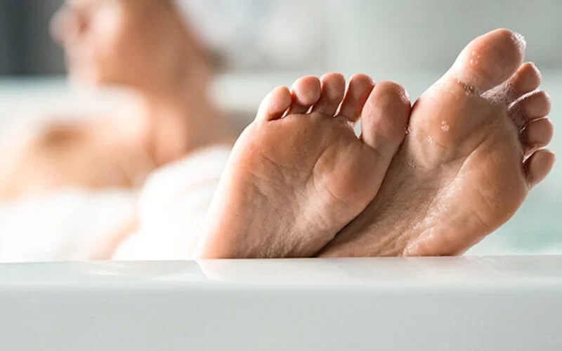 Eine Frau liegt in der Badewanne und streckt die Füße aus.