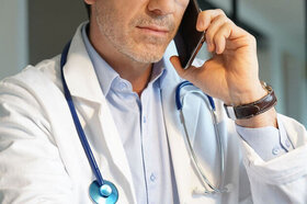 Ein Arzt hält mit der linken Hand ein Smartphone an sein Ohr. Die Fachärzte von AOK-Clarimedis beraten AOK-Versicherte kostenfrei.