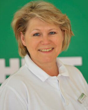 Man sieht ein Portrait einer Frau (Dr. med. Brigitta Keßler), die vor einem grünen Hintergrund steht und weißes Hemd trägt.
