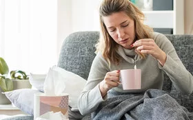 Frau sitzt erkältet auf dem Sofa und versucht mit Omas Hausmitteln gesund zu werden.