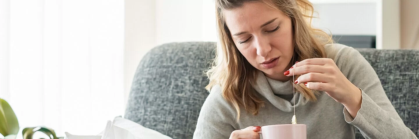 Frau sitzt erkältet auf dem Sofa und versucht mit Omas Hausmitteln gesund zu werden.