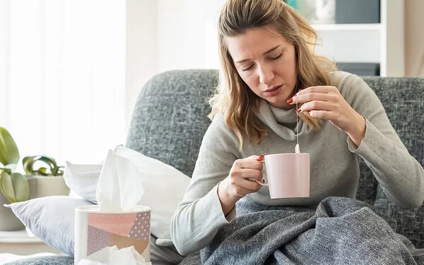 Frau sitzt erkältet auf dem Sofa und versucht mit Omas Hausmitteln gesund zu werden.