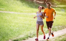Eine junge Frau und ein junger Mann joggen in der Natur und lächeln einander an.