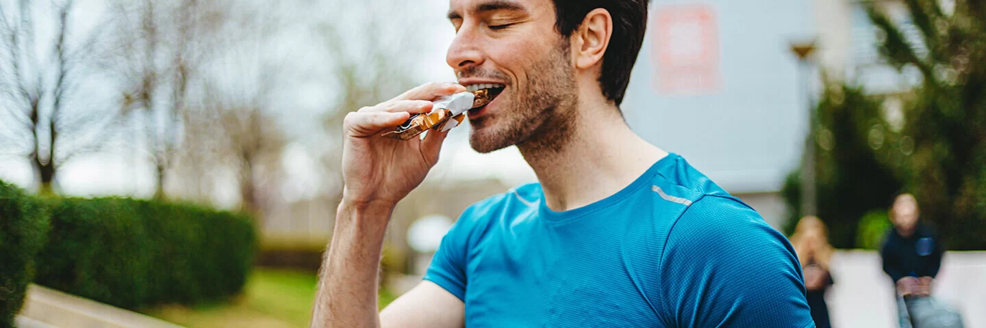Ein männlicher Sportler isst nach dem Joggen einen Proteinriegel.