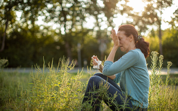Eine Frau mit Heuschnupfen und allergischem Asthma sitzt auf einer Wiese.