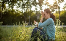 Eine Frau mit Heuschnupfen und allergischem Asthma sitzt auf einer Wiese.