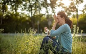 Eine Frau mit Heuschnupfen und allergischem Asthma sitzt auf einer Wiese.