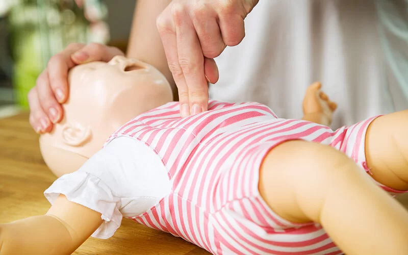 Anhand einer Puppe wird die Herzdruckmassage mit zwei Fingern bei Babys vorgeführt.