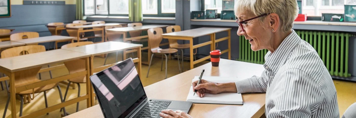 Eine Frau arbeitet mit ihrem Laptop im Klassenzimmer. Sie meldet sich für die Henrietta-Programmeinführung an.