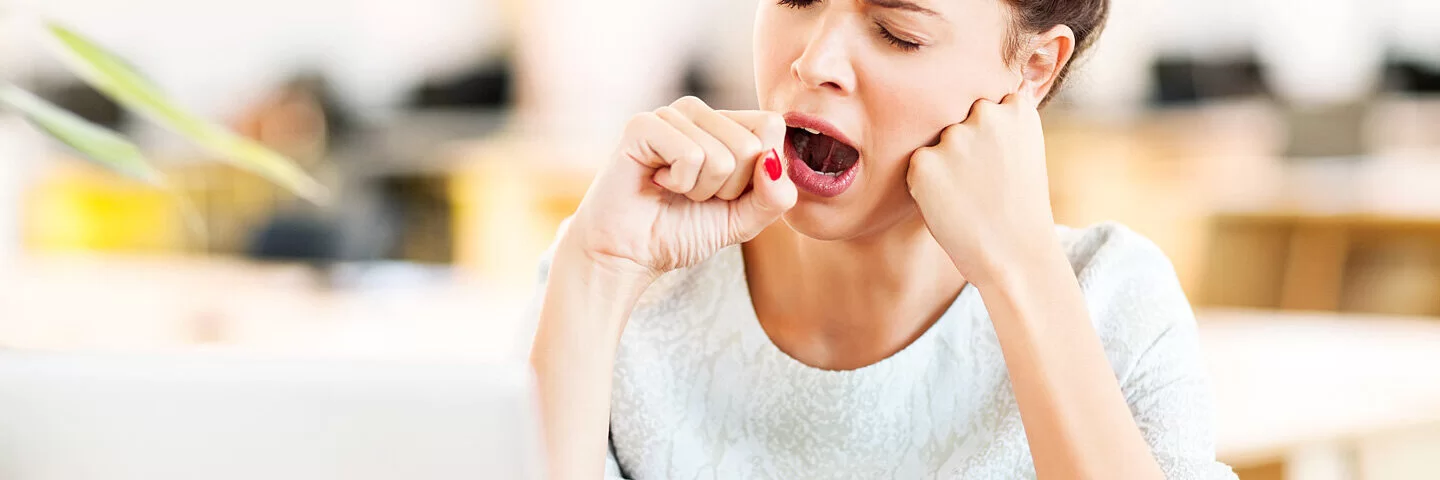 Eine junge Frau gähnt im Büro, weil sie unter Jodmangel leidet.