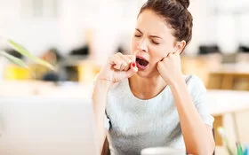 Eine junge Frau gähnt im Büro, weil sie unter Jodmangel leidet.